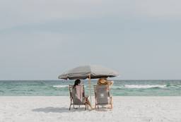 Two beach chairs under a gray umbrella facing the surf