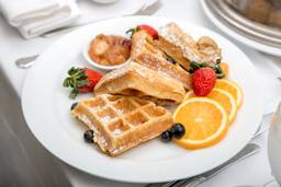 A plate of waffles with fresh strawberries and orange slices